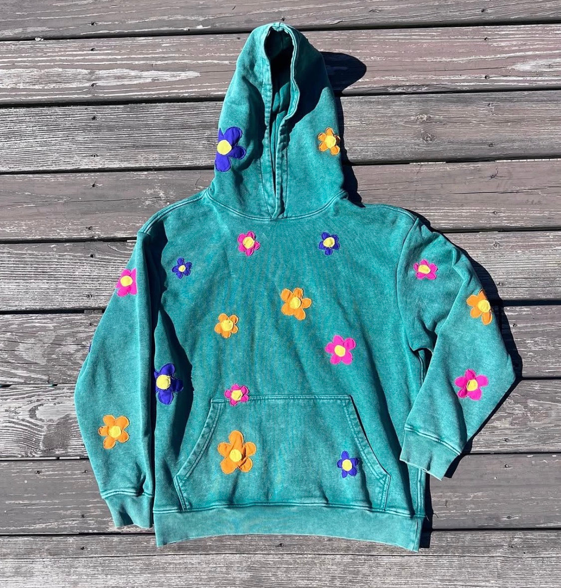 A green reconstructed hoodie with colorful floral appliqués from the Alexandra George collaboration.