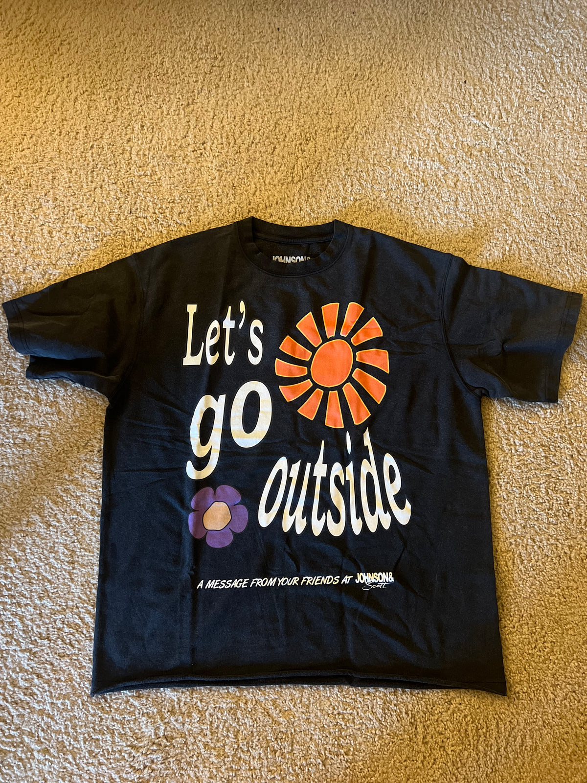 Front flat lay of black Let's Go Outside T-Shirt with orange flower graphic