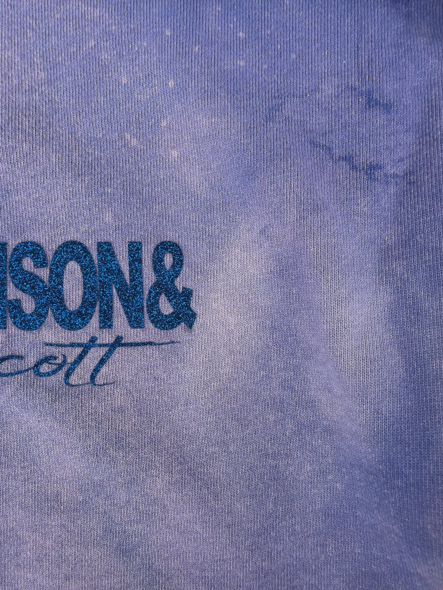 Close-up of marble bleach fade and blue glitter JOHNSONANDSCOTT signature on the hoodie